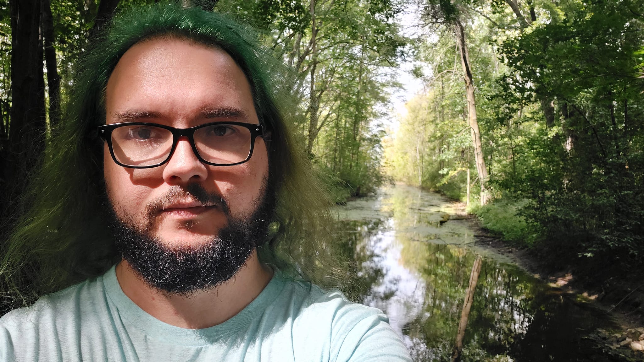 A man with green hair stands on a dam with a channel extending behind him, Photo 1